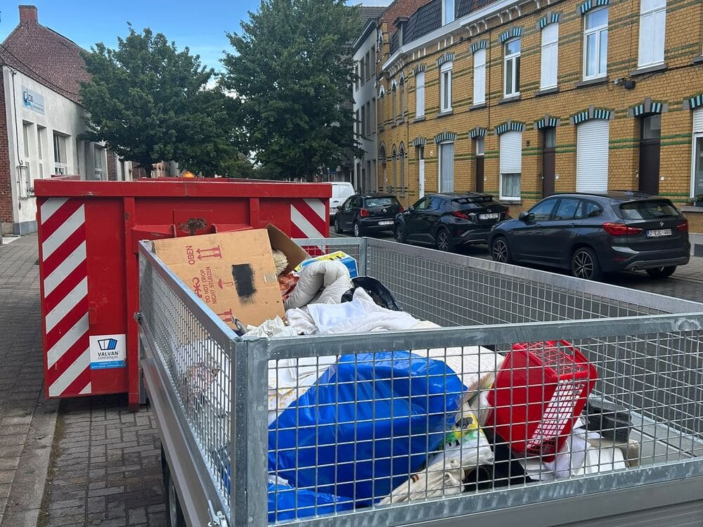 Een container en een aanhangwagen voor de deur in een straat.